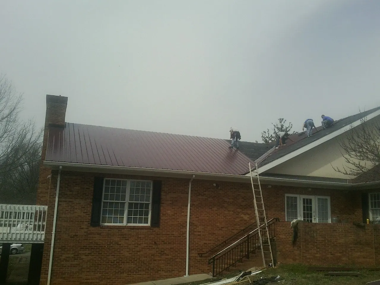 Crew setting red metal roofing panels on a brick home in Sandown