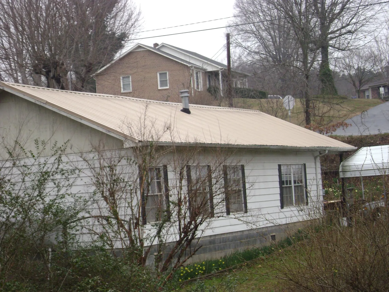 Tan metal roof on a white sided house set into a hillside — Commercial Roofing by Roofing Brothers in Sandown
