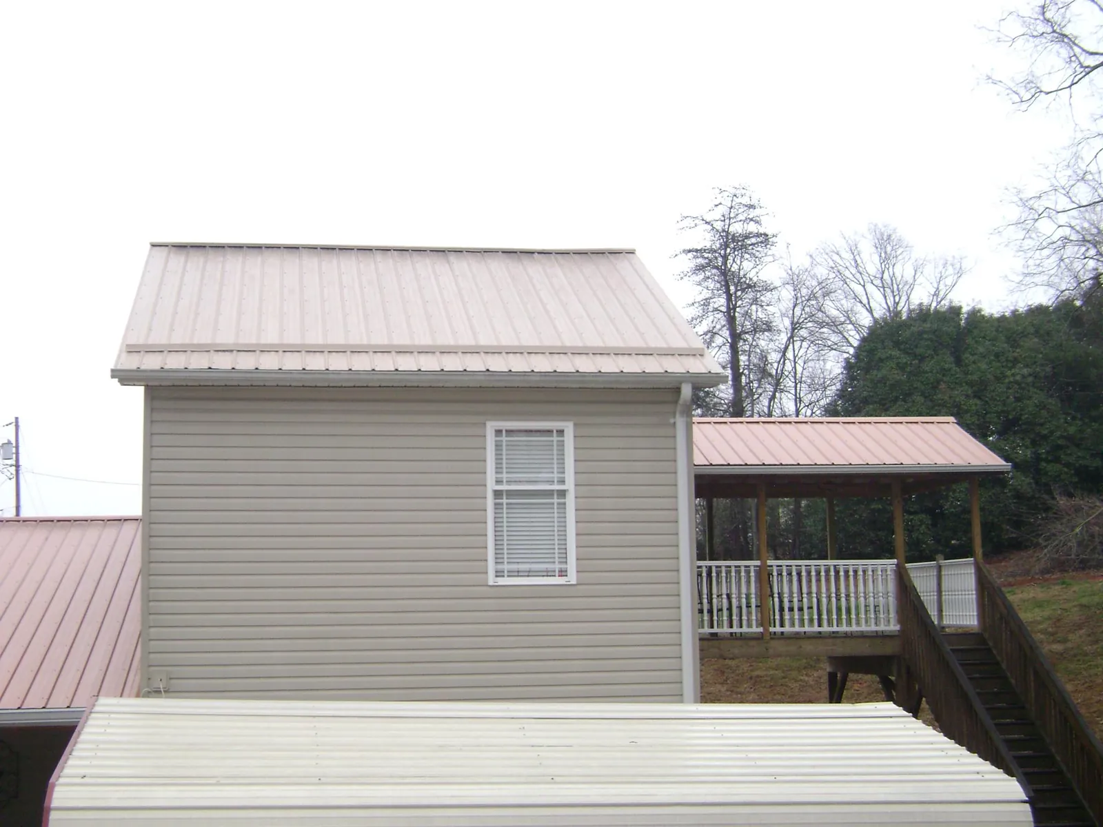 Tan metal roofs on a two story addition and attached porch, from a Roof Replacement job in Sandown